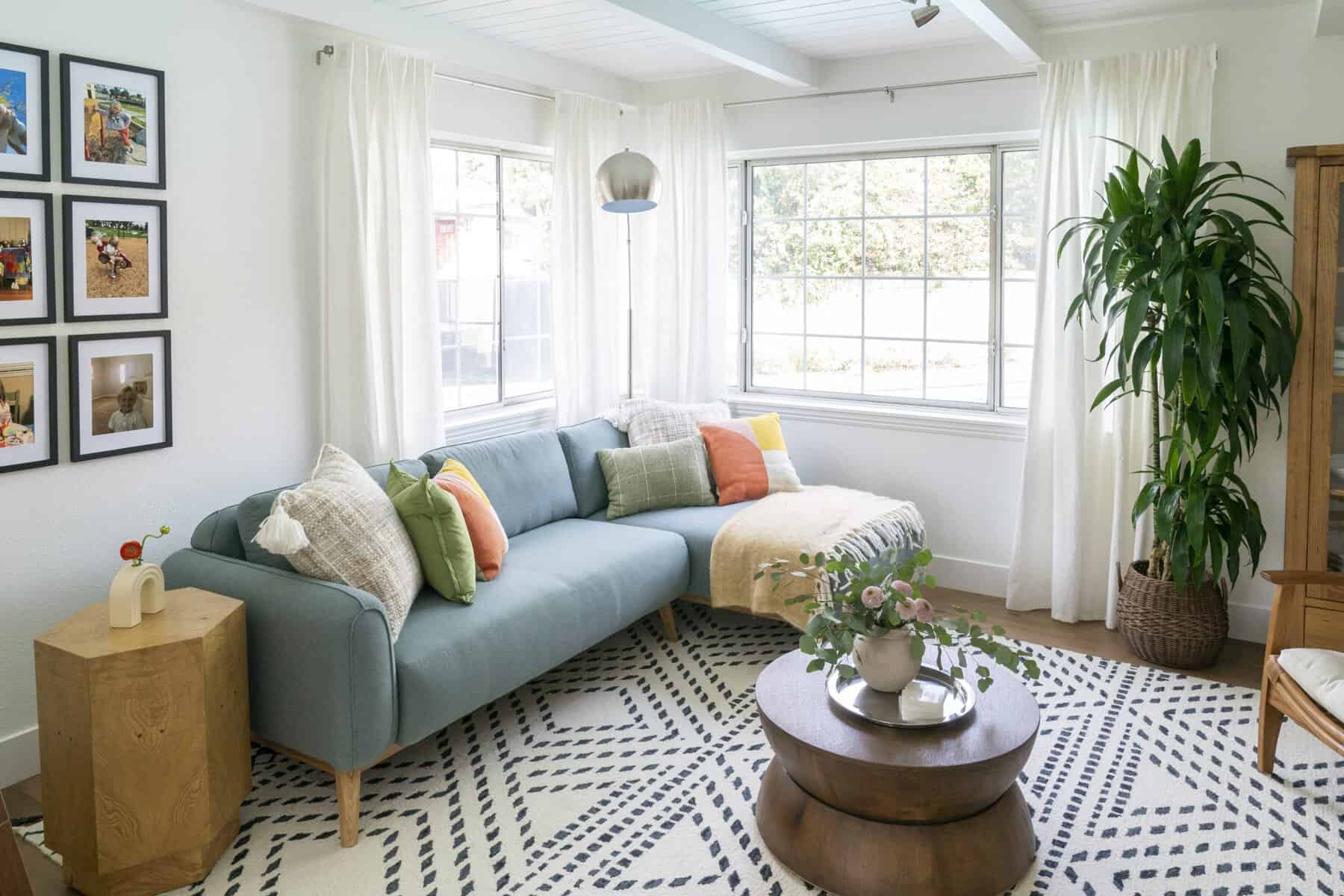 Bright living room with blue sectional sofa, colorful pillows, round wood coffee table, and large windows