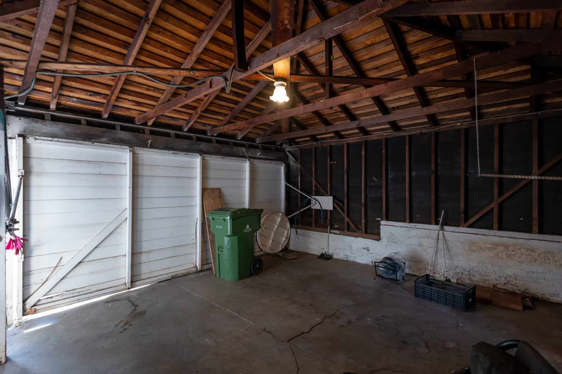 Old garage interior with exposed beams, concrete floor, and minimal storage items