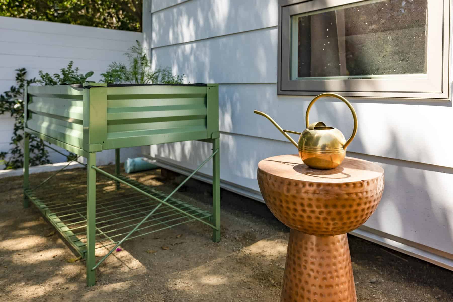Outdoor planter box with herbs next to a copper side table holding a gold watering can