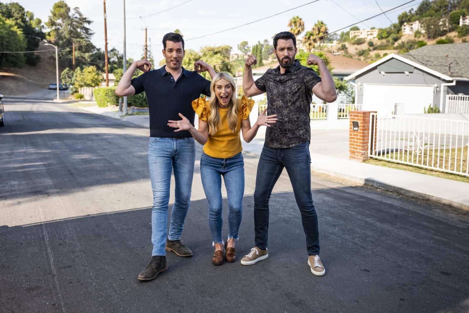 Drew and Jonathan Scott posing playfully with a woman on a suburban street